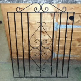 Black metal side gate with decorative scroll top design, shown with fixing brackets. Powder-coated and suitable for garden or side access.