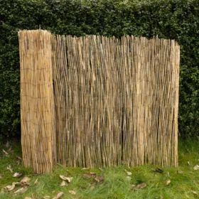 A far view of a partially unrolled roll of reed screening against a garden hedgerow.