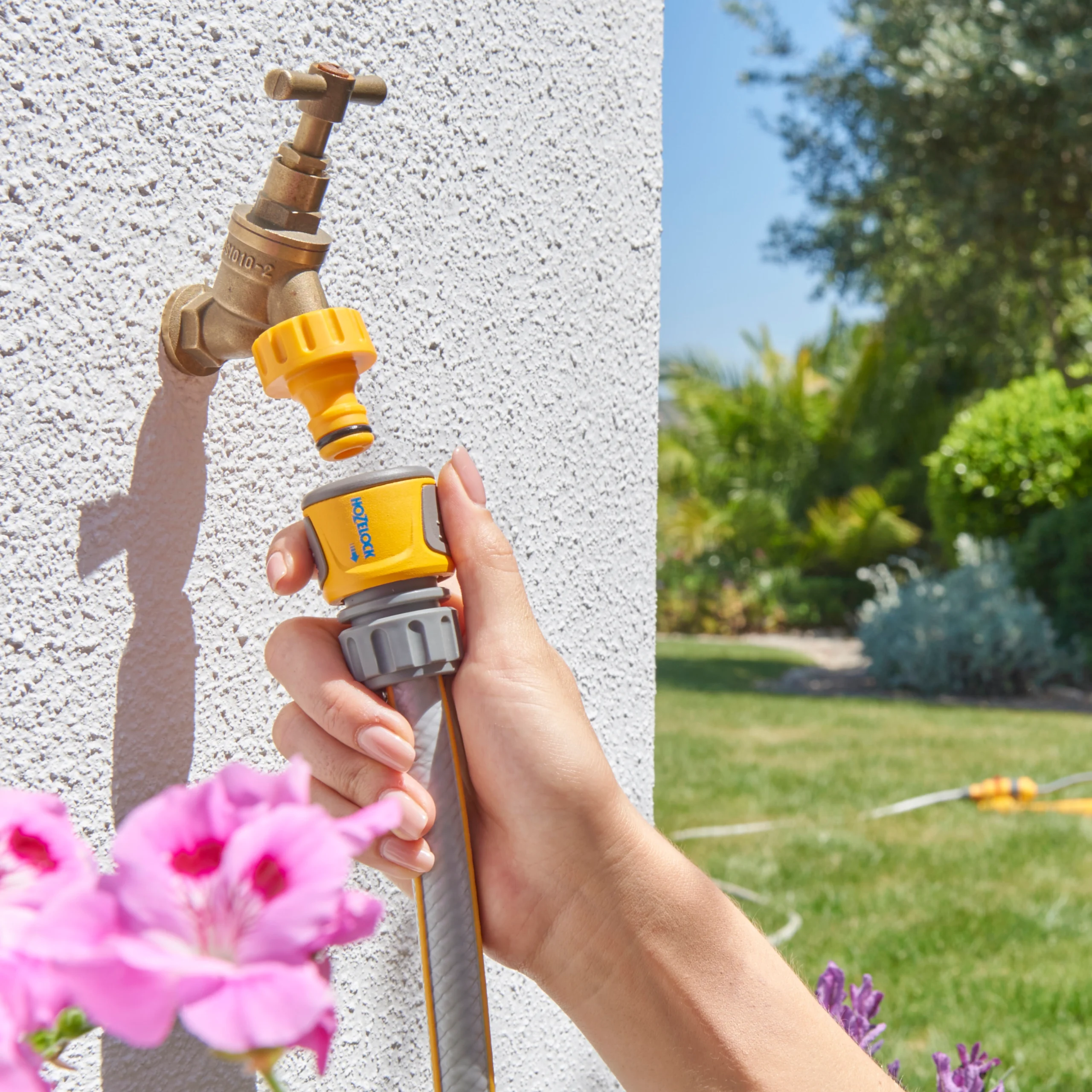 The Hozelock Standard Soft Touch Hose End Connector being used to connect a hose pipe to an outdoor tap in a garden