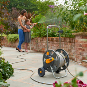 The Hozelock hose cart with an unreeled hose being used to water bushes in a garden