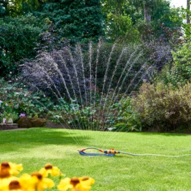 The Hozelock Rectangular Sprinkler Pro 350 L being used in a garden spraying water in a fan shape