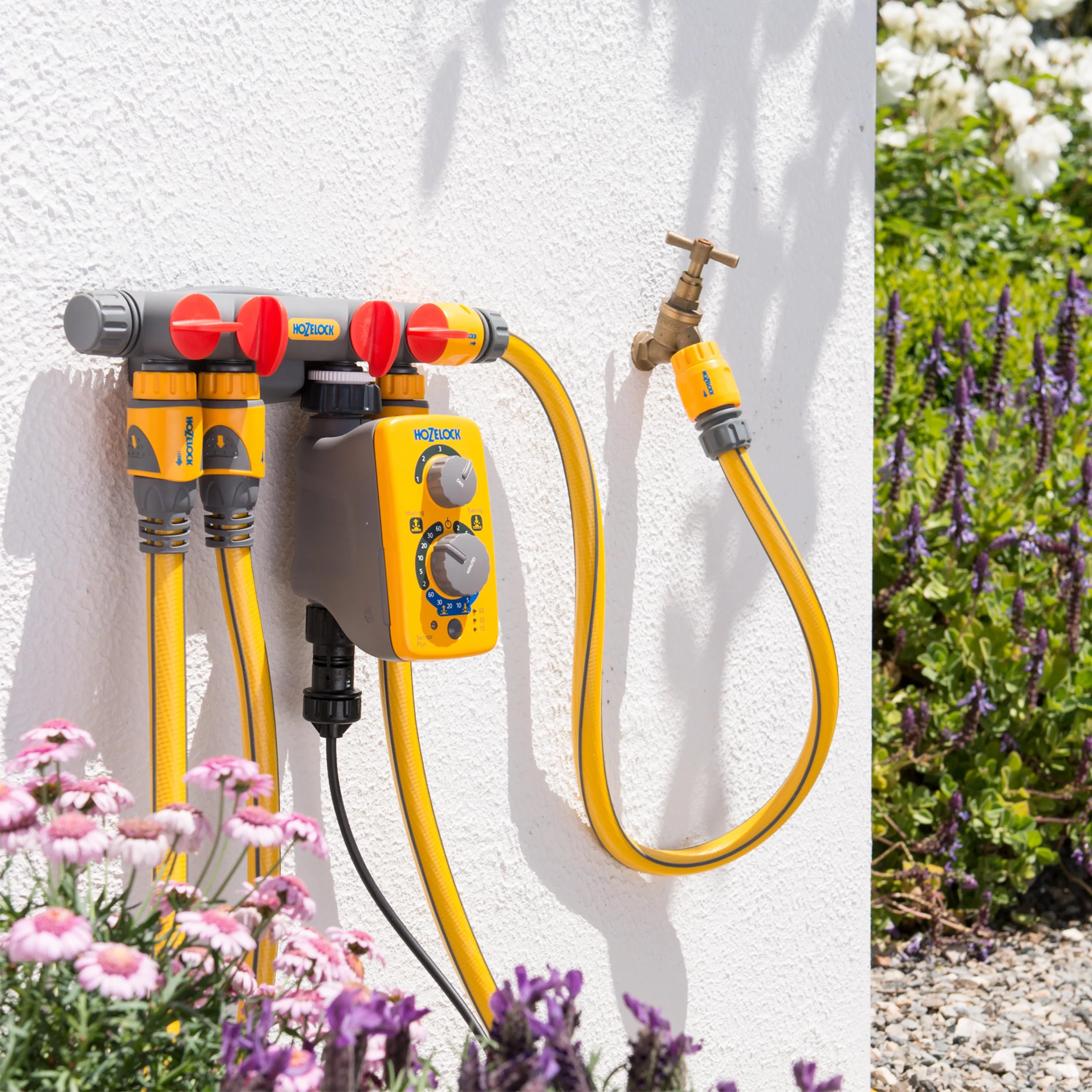 A Hozelock 4 way tap connector hooked up against a wall with some hoses attached to the additional connectors