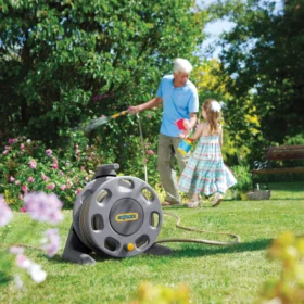 The Hozelock Compact Reel with a 25m hose being used in a green garden to water some plants in the background
