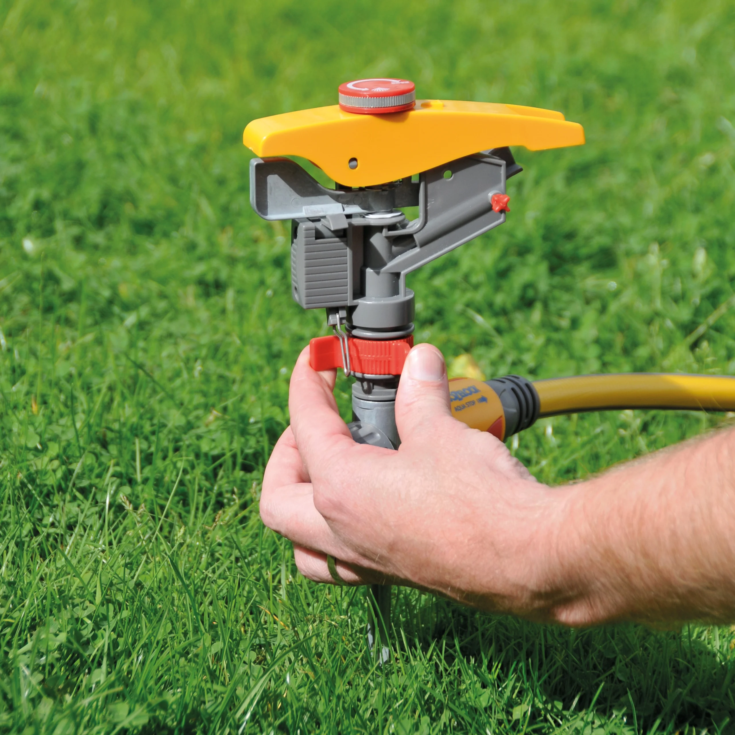 Step 3 for the Hozelock Pulsating Sprinkler controls shown with a hand flipping a metal trip lever against red arc adjustment rings