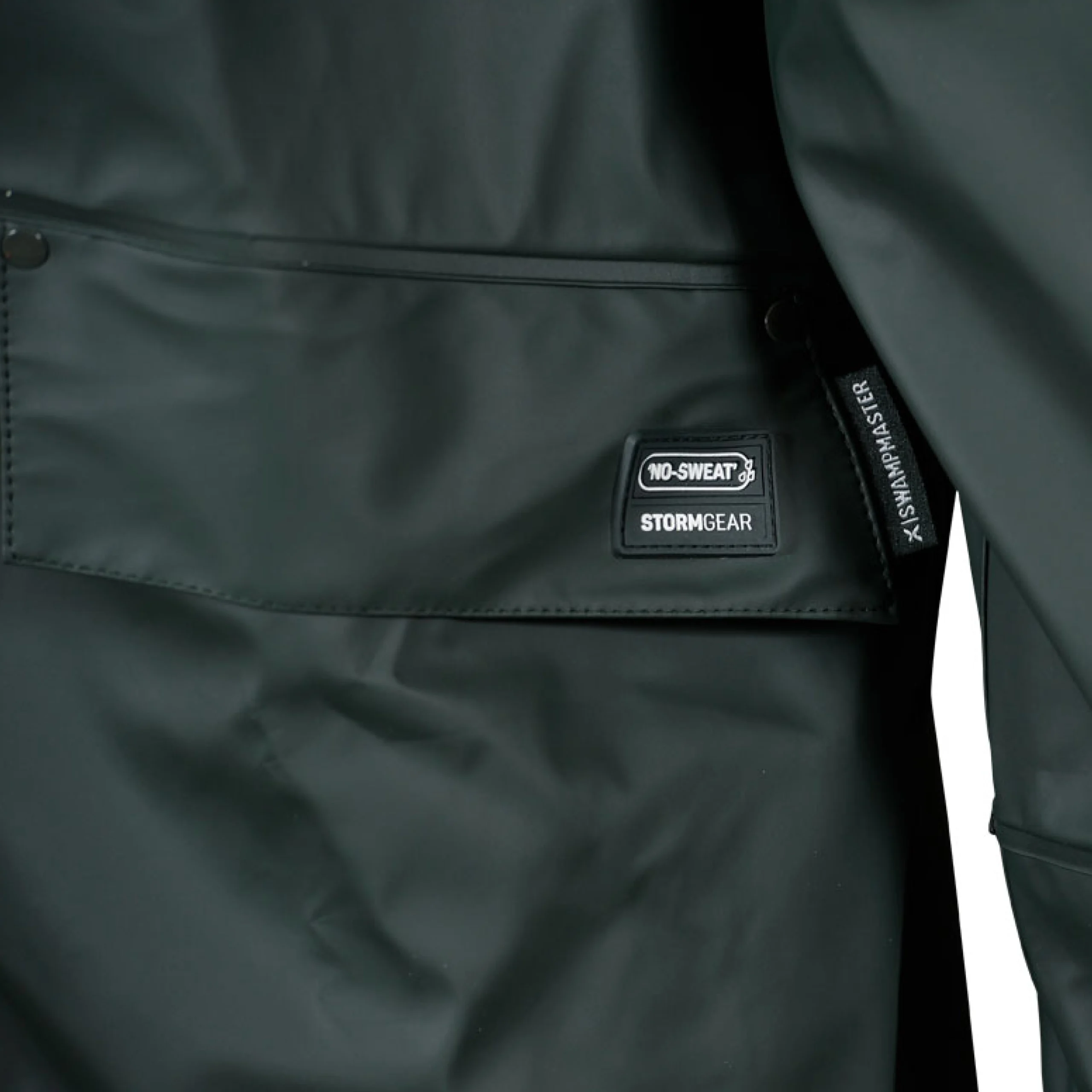 Close-up of pocket detail on green waterproof jacket featuring No-Sweat Stormgear branding and flap closure – durable outerwear for wet and rugged conditions.