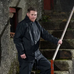 Man wearing navy waterproof jacket and trousers outdoors on wet stone steps – rugged rainwear designed for tough weather conditions and active work environments.