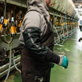 Person wearing Swampmaster milking sleeves in a dairy parlour – protective green arm covers designed for comfort and durability during milking routines.