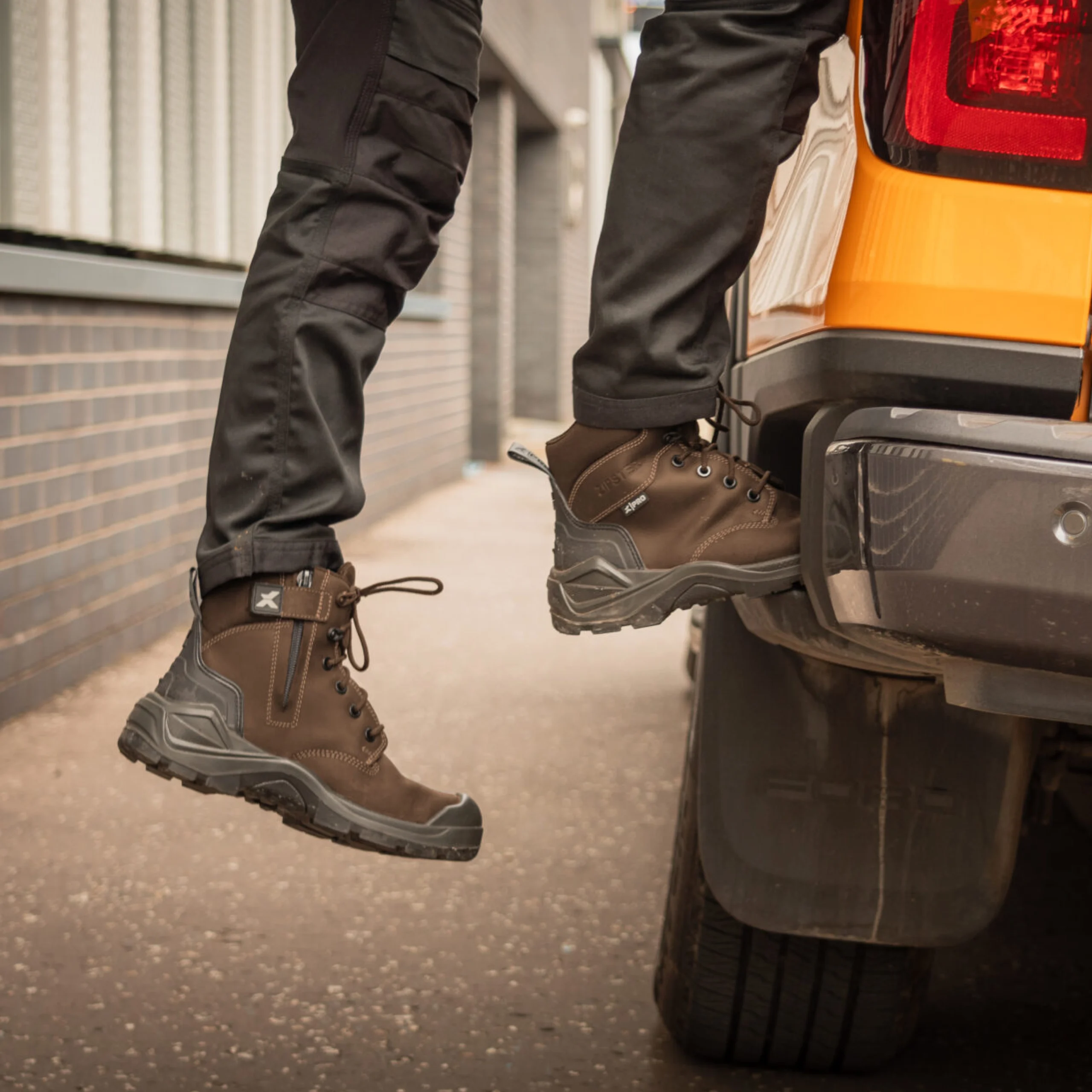 Person wearing brown work boots climbing onto the back of a pickup truck, showcasing durable safety footwear ideal for construction and trade environments.