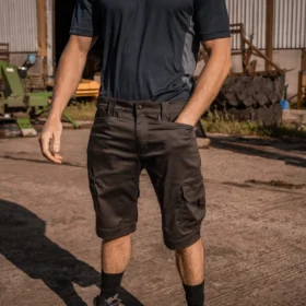 Man wearing grey and black work shorts with cargo pockets in an outdoor industrial setting, demonstrating comfortable and durable summer workwear.