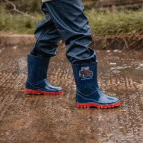 Child wearing Swampmaster blue tractor wellies with red soles splashing in puddles, waterproof PVC kids boots for outdoor adventures.
